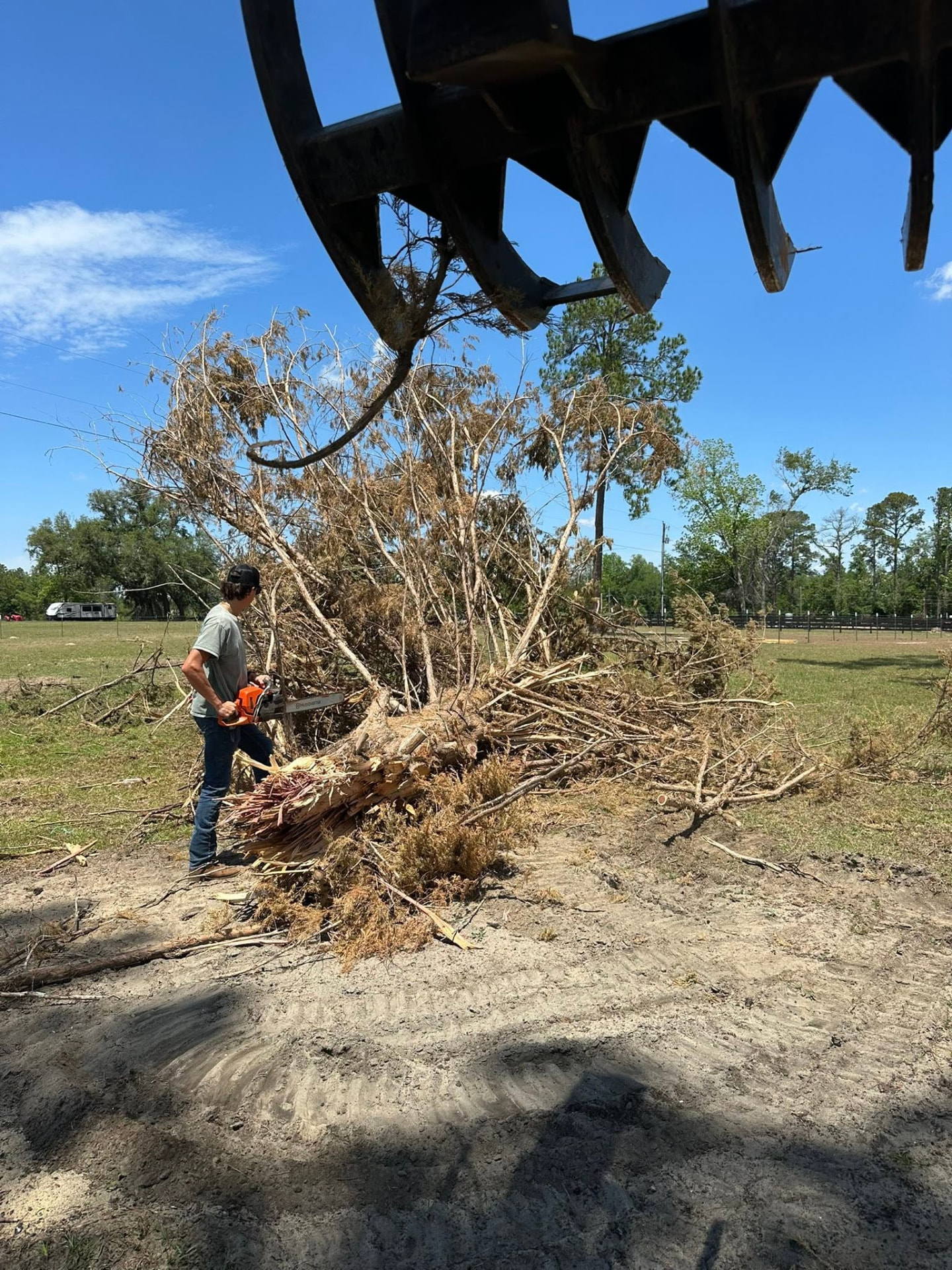 Grapple loading brush while a worker runs a chainsaw